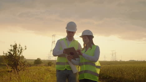 ingeniería trabajando en la torre de alta tensión comprobar la información en la computadora tablet dos empleados hombre y mujer