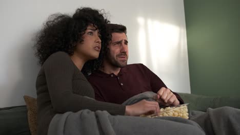 couple having popcorn and watching scary movie at home