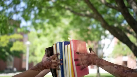 a group of students with henna designs on their hands joyfully toss colorful notebooks into the air in a lively outdoor environment. their celebration reflects achievement and camaraderie.