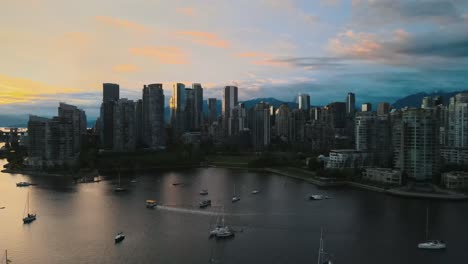 drone establishing shot of vancouver skyline with cruising boats in river during golden sunset in canada - panning shot