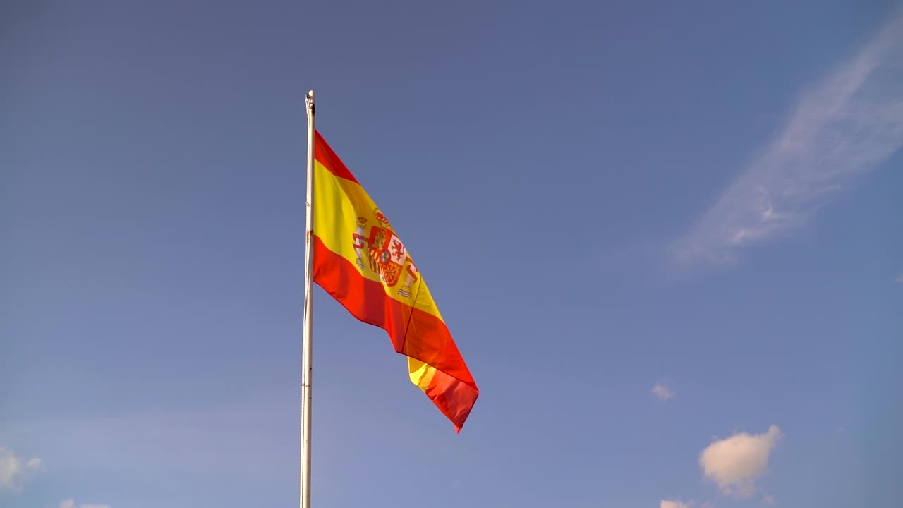 Bandeira espanhola vibrante e colorida tremulando contra o céu azul com poucas nuvens em câmera lenta