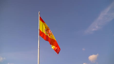 vibrant and colorful spanish flag waving against blue sky with few clouds in slow motion