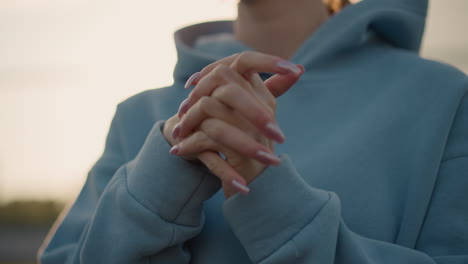 close-up of lady with polished nails performing wrist twist, wearing blue sweater, showing hands in focus with soft background, elegant hands and wrist movement in fitness routine