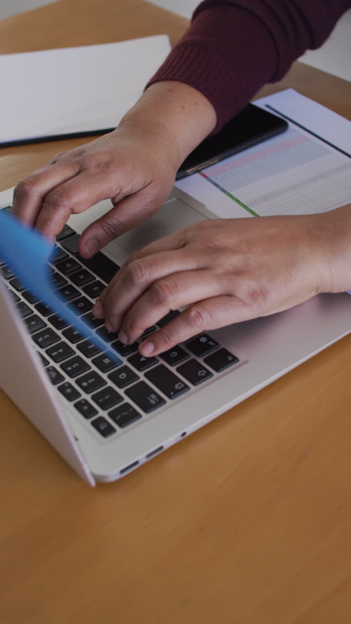 video vertical de las manos de una mujer afroamericana mayor en el escritorio escribiendo en el teclado de la computadora portátil