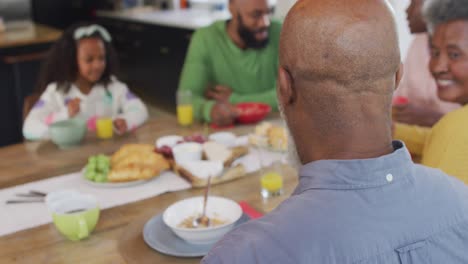 video de un feliz abuelo afroamericano girando y sonriendo en la mesa del desayuno familiar