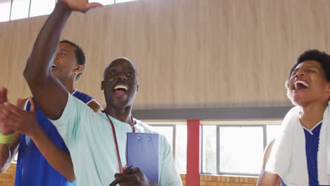 Diverse-male-basketball-team-and-coach-celebrating,-smiling-and-high-fiving-together