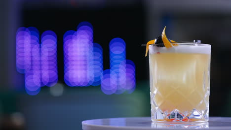 beautifully decorated cocktail in the wide glass on the rotating white table. beverage served in the bar. close up. blurred backdrop.