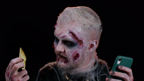 hombre siniestro zombie de halloween usando tarjeta de crédito y teléfono inteligente mientras compra compras en línea