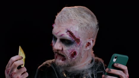 unheimlicher mann halloween-zombie mit kreditkarte und smartphone beim online-einkauf