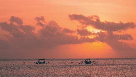 silhouetted outrigger balinese boats in a sea with bright sun behind clouds, bali indonesia - slow motion