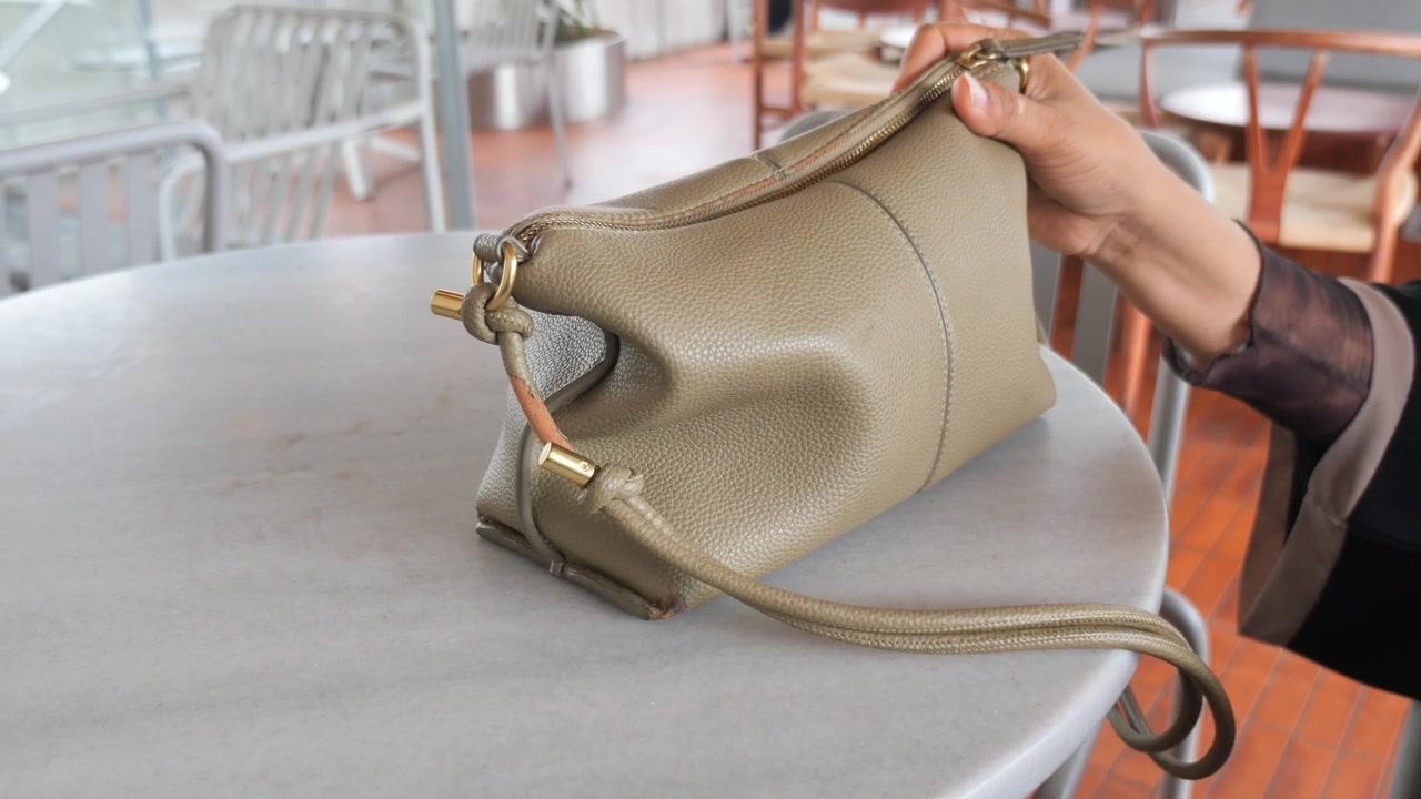 Mano che prende una borsa in pelle beige da un tavolino da caffè