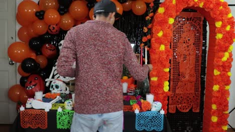 mexican man placing sugar skulls on decorated día de muertos altar