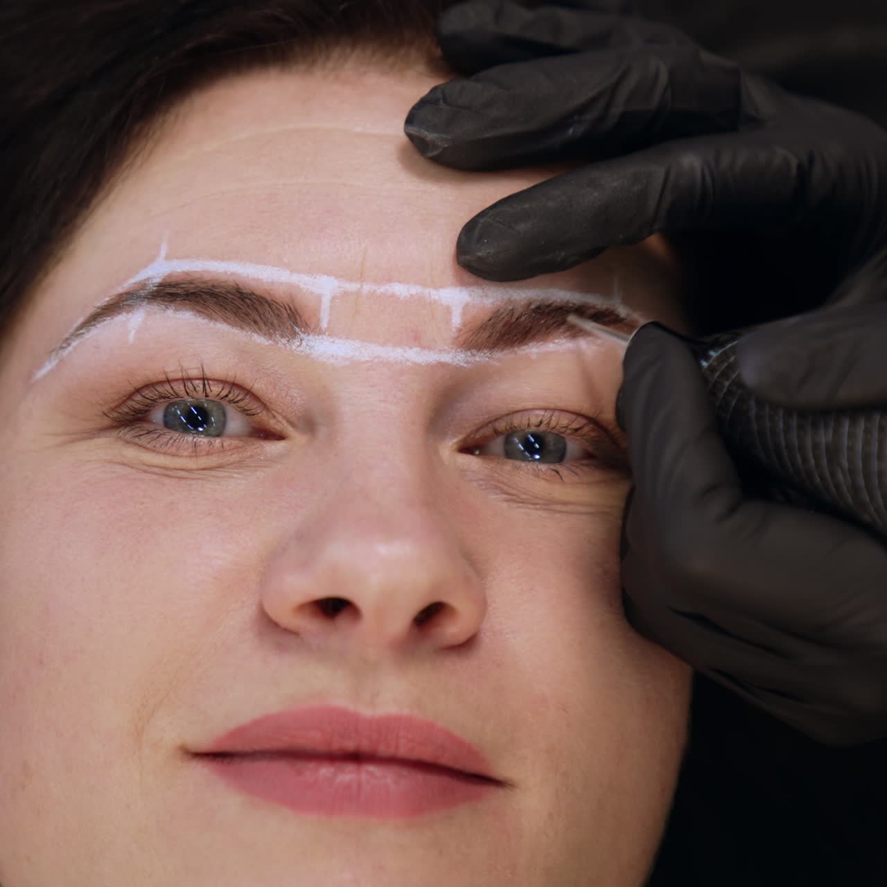 Hands of cosmetologist in black gloves hold the special tool for permanent eyebrow make up. Close up. Blurred backdrop