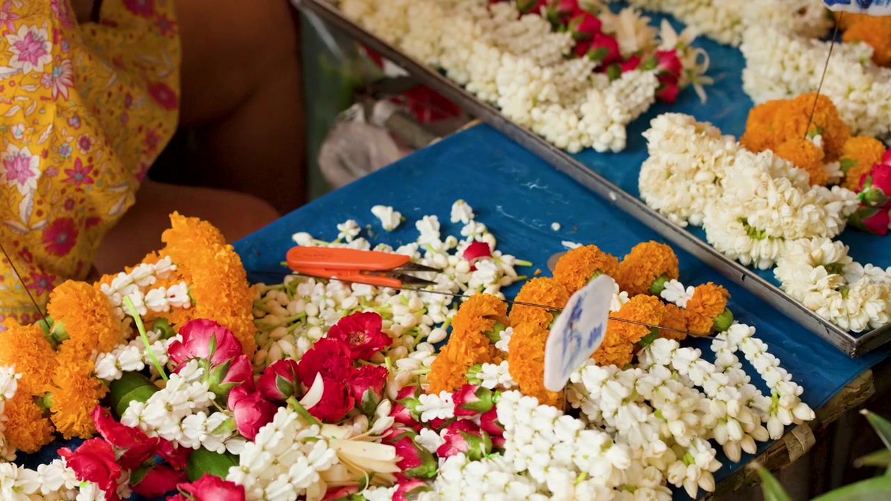 Primo piano di un fiorista che sistema ghirlande di gelsomino e calendule al famoso mercato dei fiori di Bangkok.