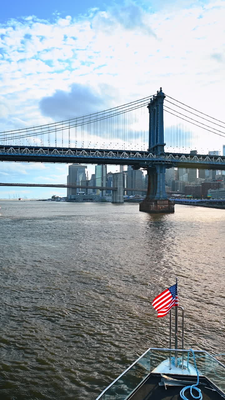 Viaggio a bordo di una barca con bandiera americana a prua sull'East River. Il Ponte di Manhattan e il Ponte di Brooklyn. Video verticale.