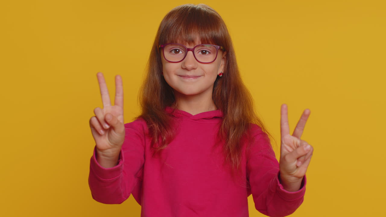 Felice bambina preadolescente che mostra il segno della vittoria, sperando nel successo e nella vittoria, facendo il gesto di pace.