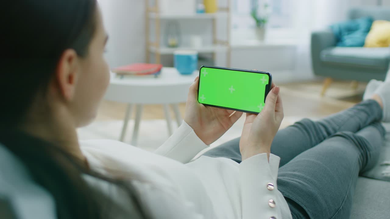 집에서 소파에 누워있는 여성이 스마트폰을 사용하여 풍경 모드에서 수평으로 들고 있습니다. 화면에는 추적 마커가 있습니다.