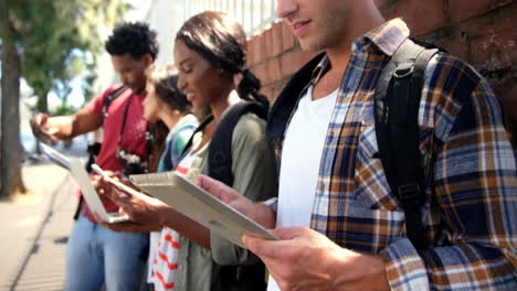 friends leaning against wall using digital tablet