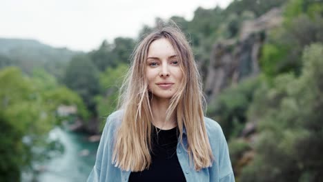 Portrait-of-beautiful-woman-standing-in-front-camera---high-green-hills-and-river-on-background