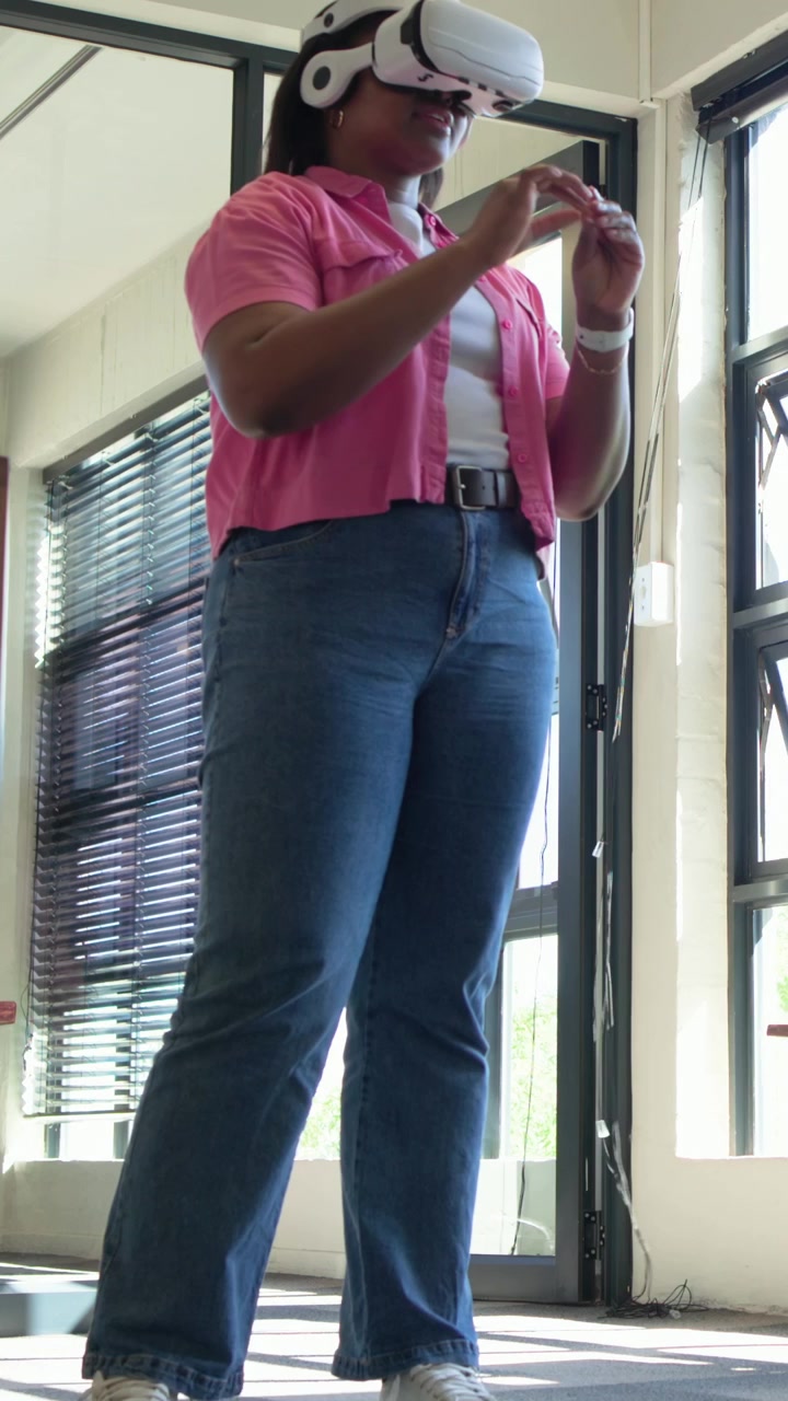Vertical video: Headset activating, woman in pink shirt pinching near window using white VR headset