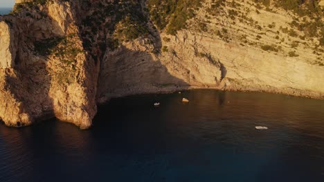 aerial shot starting big and descending onto a group of people partying in a boat along the ibiza cliffs