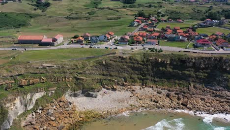 aerial shot on the coast of the cantabrian sea towards the cliff there is a road on which cars pass next to typical houses in green meadows with the sky in the background and clouds in cantabria spain