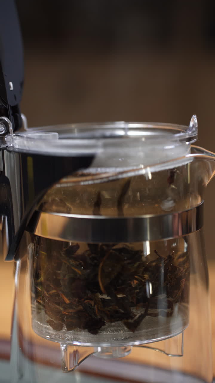 verter agua caliente en una tetera de vidrio con hojas de té