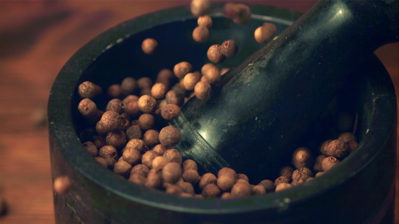 Grani di pimento che cadono in un mortaio e pestello al rallentatore