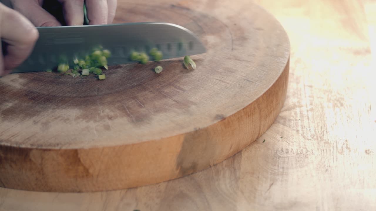 두꺼운 나무 도마 위에 봄 양파를 자르는 요리사 칼로 요리사 손의 슬로우 모션 슬라이더 샷