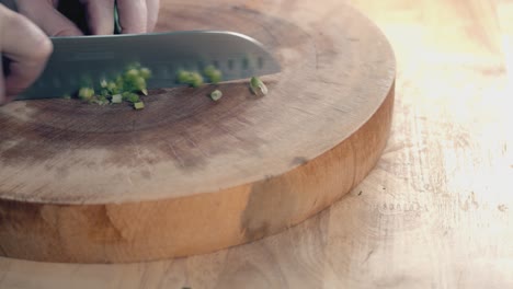 toma de control deslizante en cámara lenta de las manos de los chefs con un cuchillo de chef cortando cebolletas en una gruesa tabla de cortar de madera