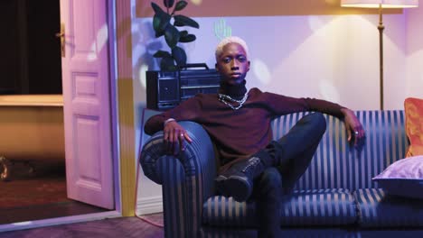 young handsome african american man entering a retro room, sitting on couch and looking at camera