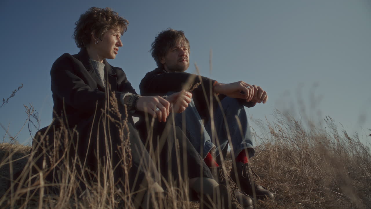 Couple Sitting in Tall Dry Grass under Clear Sky, Discussing Scenery of Nature