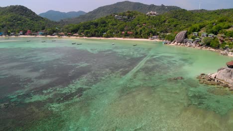 Aerial-view-of-Koh-Tao's-emerald-colored-beach,-with-mountains-and-forests-at-the-shore