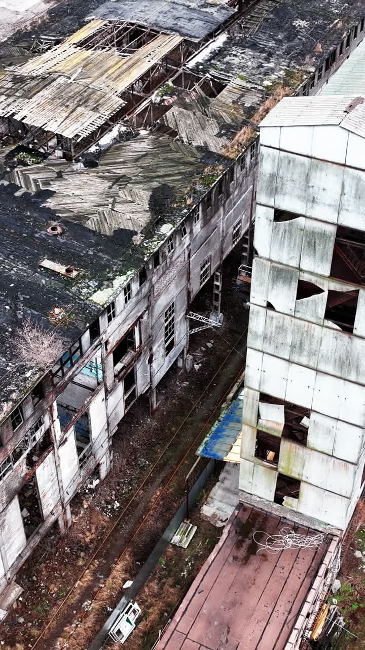 Empty boxes of an old plant buildings. Damaged roofs and walls of industrial architecture. Premises still in use at the backdrop. Vertical video