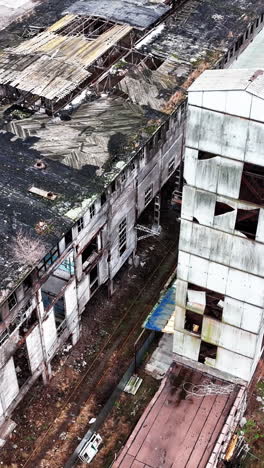 Empty boxes of an old plant buildings. Damaged roofs and walls of industrial architecture. Premises still in use at the backdrop. Vertical video