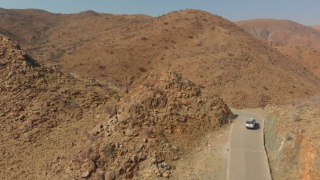 Seguimiento-Aéreo:-Panorámica-Hacia-Abajo-Sobre-El-Vehículo-Que-Gira-En-Una-Carretera-Estrecha-En-Las-Montañas-Del-Desierto