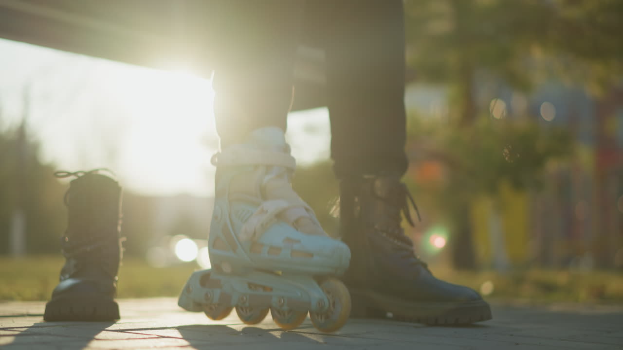 A close-up shot of a person wearing a rollerblade on one foot, with the wheels in motion, stepping on the ground in a park . The other foot is in a black boot, and another black boot is placed nearby