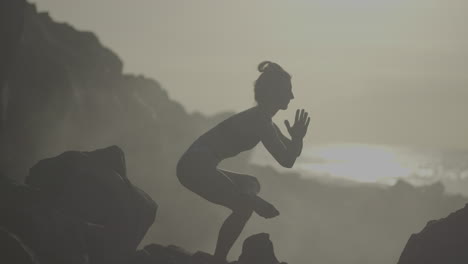 woman practicing yoga on rocky beach at sunrise