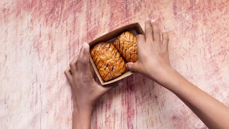 hands holding pastries in a brown box