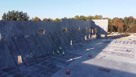 una larga foto de camiones de drones de hombres asegurando abrazaderas de soporte en paneles de hormigón en un sitio de construcción