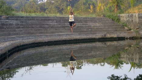 girl doing tree pose vrhsasana double image reflection in still water on steps of lade