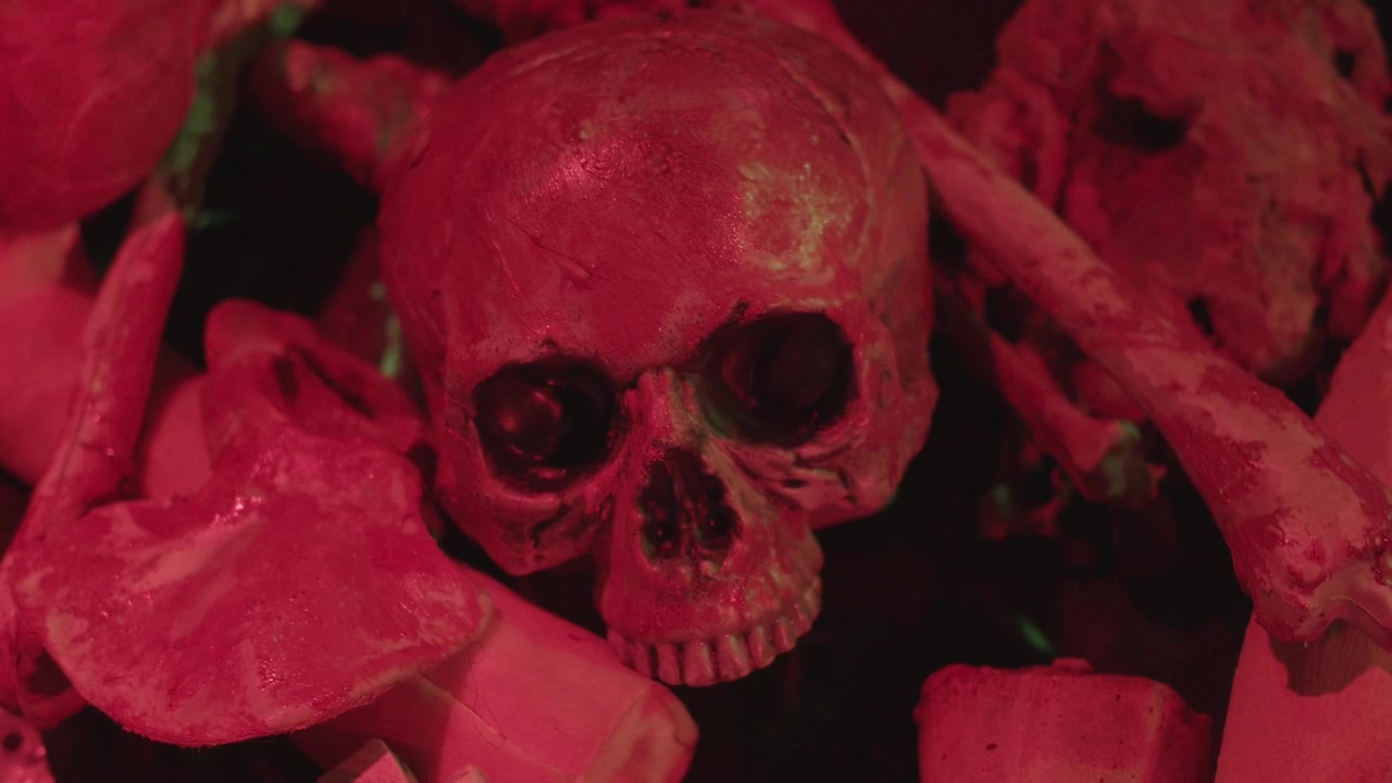 Prop skull and human like bones pile illuminated by eerie red light, dolly focus