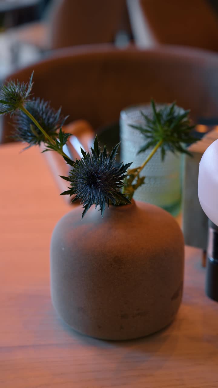 Détail d'une fleur d'Eryngium dans un vase en grès avec un arrière-plan flou (bokeh). Gros plan d'une plante de chardon bleu dans un petit vase en céramique sur une surface en bois clair dans un café.