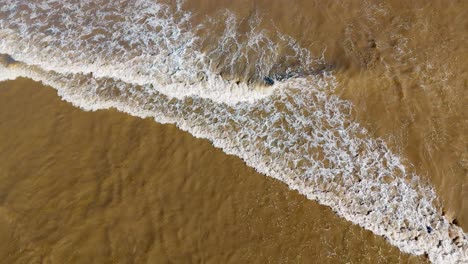 aerial footage of waves gently breaking on the beach, with golden sand