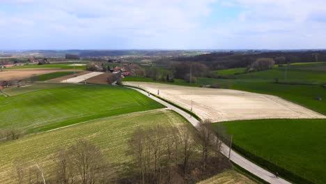 Aerial-tilt-down-with-cyclist-on-their-biking-vacation-between-Belgian-agricultural-fields-on-a-cloudy-day