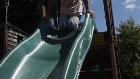 adorable four year old girl climbing playframe to use slide in garden