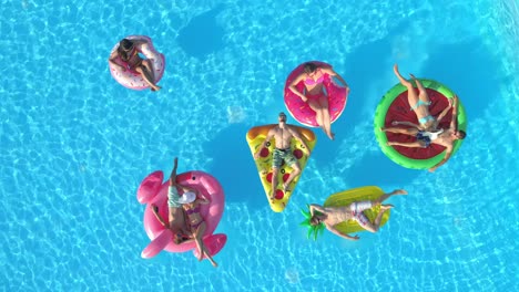 drone: tourists relax on colorful floaties while enjoying a sunny day at pool.