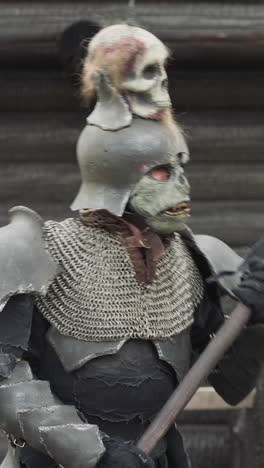 medieval monster in knight armor walks along fence surveying territory of settlement. evil warrior prepares to attack villagers closeup on blurred background