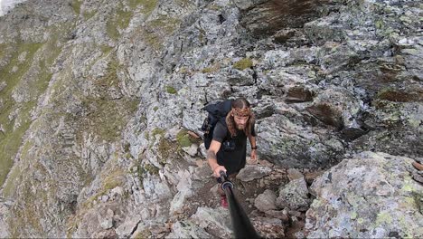 A-young,-strong-and-fit-man-with-long-hair-and-tattoos-is-walking-up-a-rocky-path-in-Switzerland-during-a-summer-day