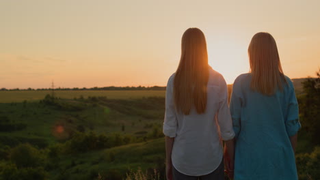 a woman with her teenage daughter admire the sunset in a picturesque valley. back view